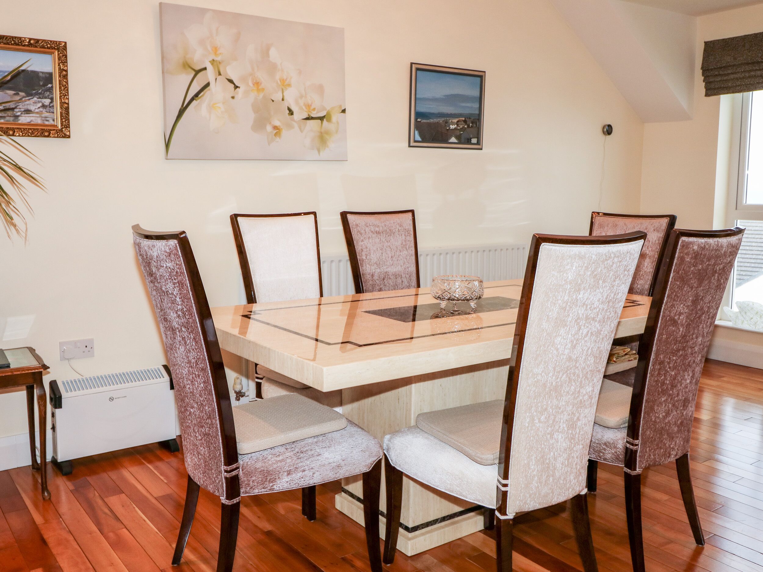 A dining area with a rectangular table, six upholstered chairs, and three framed artworks on the wall.