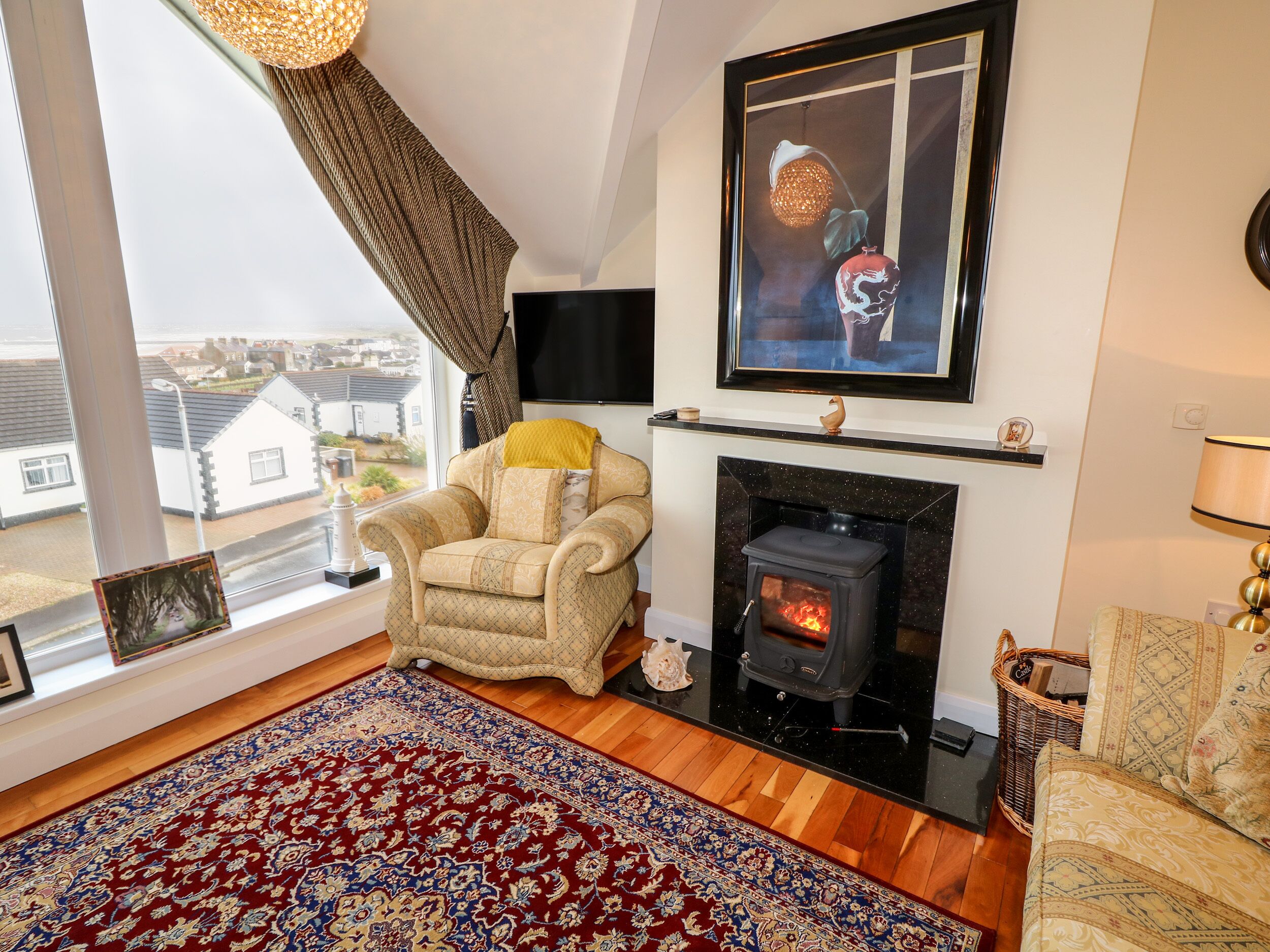 A cozy living room with a fireplace, a comfortable armchair, a large window with a view, and a decorative rug.
