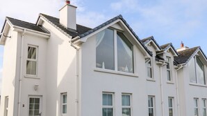 Ein weißes, zweistöckiges Haus mit großem Fensterfront, Schornstein und einer kleinen Veranda mit Treppen.