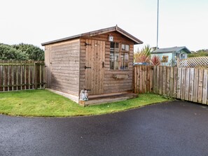 A small wooden shed with a door and windows, surrounded by a wooden fence and a grassy area.