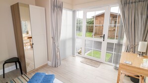 Ein Schlafzimmer mit Bett, Schreibtisch, Stuhl, Kleiderschrank und einer Glastür, die in einen Garten führt.