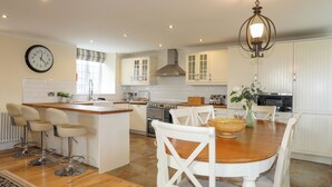 A modern kitchen with white cabinetry, a central island, and a dining area with white chairs. - Capel Hermon (Holyhead)