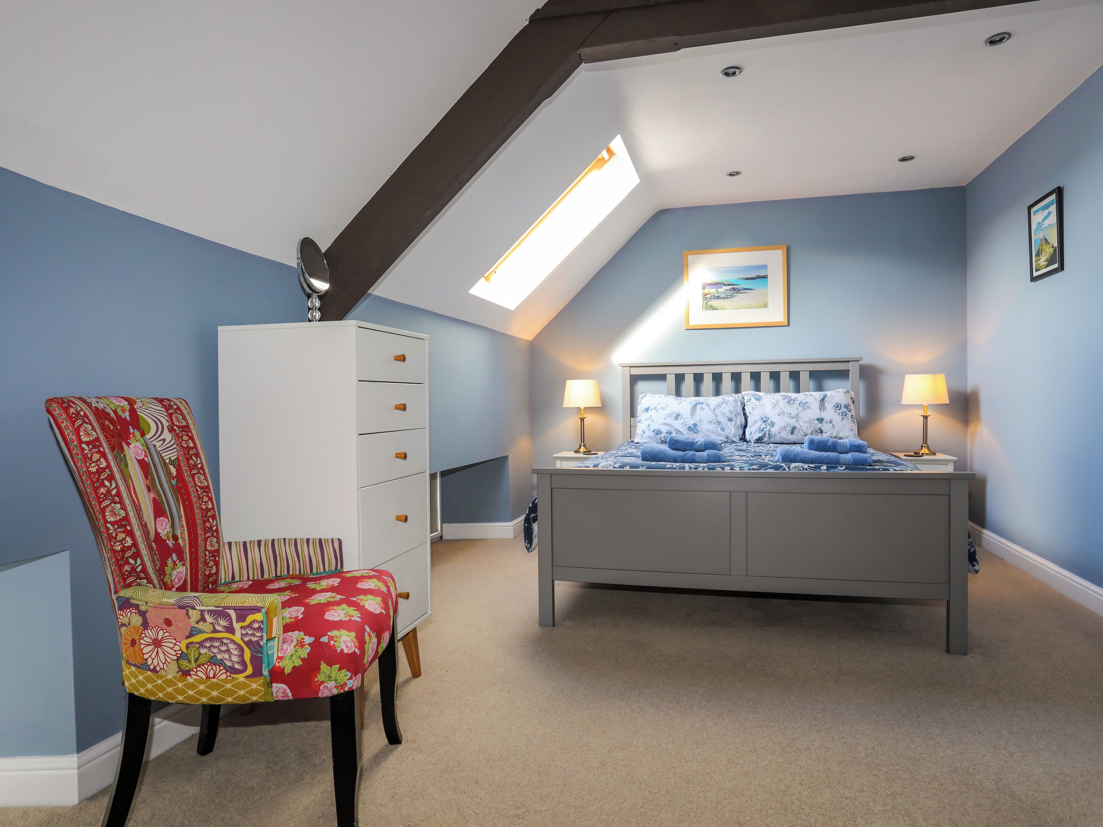 Een slaapkamer met een bed, een dressoir, een stoel en een dakraam.