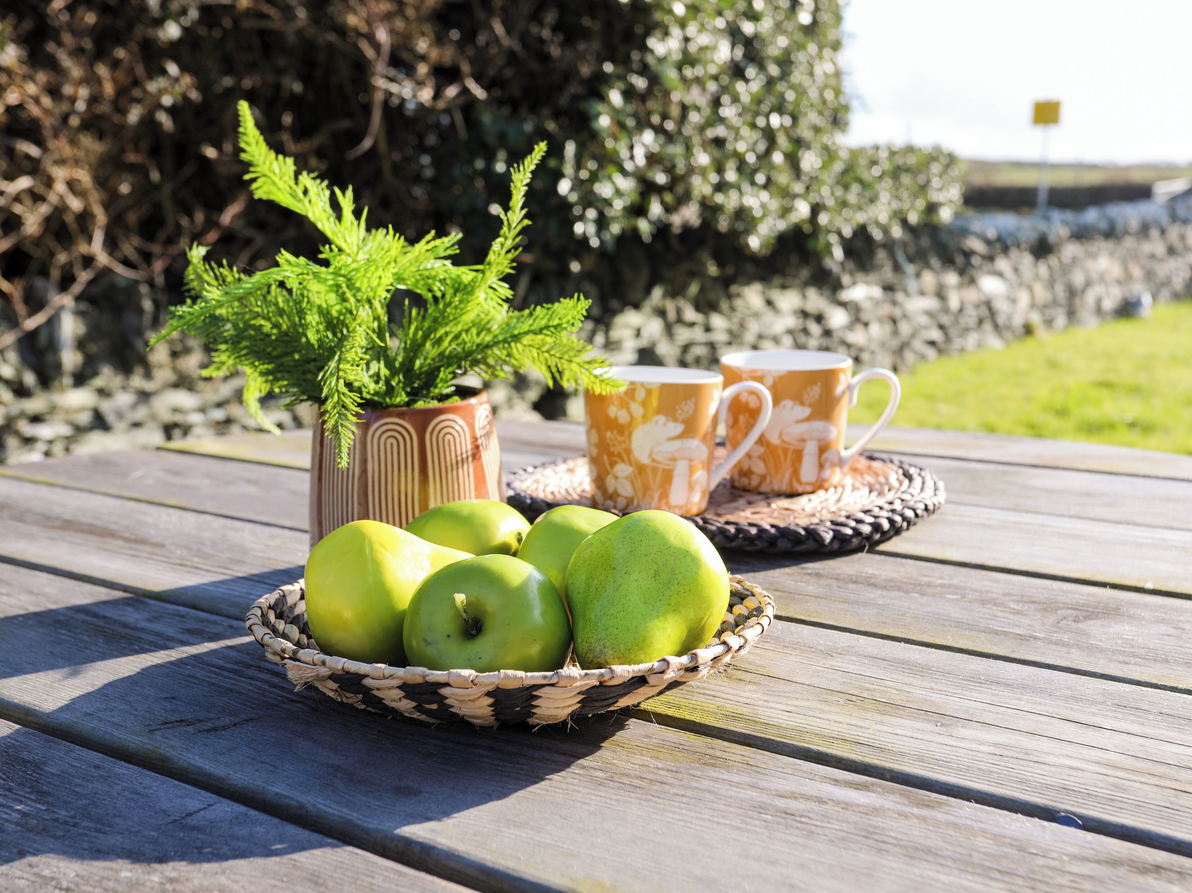 A wooden table with a woven basket containing green apples and a potted plant.