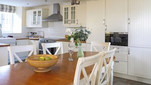 A kitchen with white cabinets, a wooden dining table, and a bowl of fruit. - Capel Hermon (Holyhead)