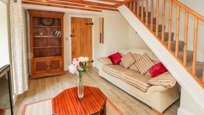Ein gemütliches Wohnzimmer mit einer Holztreppe, einem Sofa mit gestreiften Kissen, einer Holzkommode und einer Vase mit Blumen auf einem Tisch.