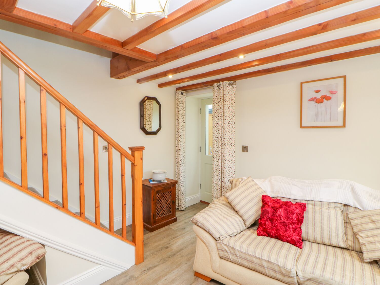 A cozy living room with a wooden staircase, a sofa with striped cushions, and a red pillow.