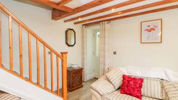 A cozy living room with a wooden staircase, a sofa with striped cushions, and a red pillow.