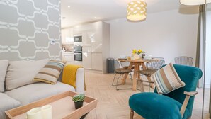 Ein modernes Wohnzimmer mit einer Couch, einem Türkis-Armlehnstuhl, einem Holztisch und einem Essbereich mit Tisch und Stühlen.