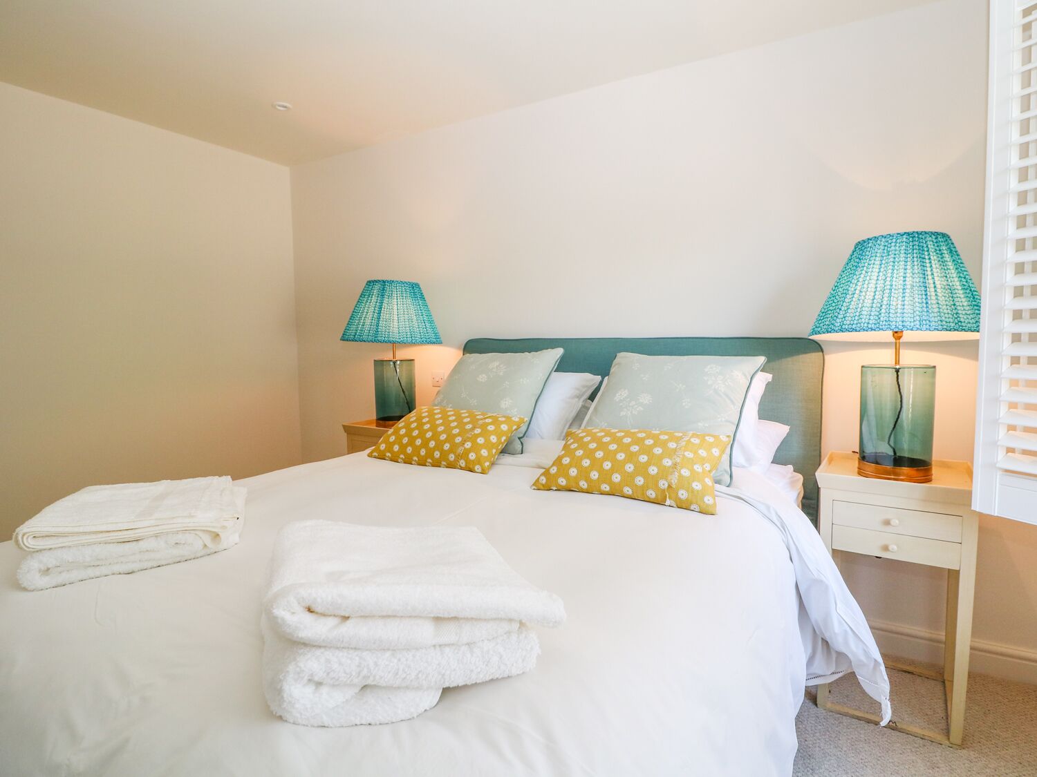 A neatly made bed with white bedding and two pillows, one yellow and one white, in a room with a teal headboard.