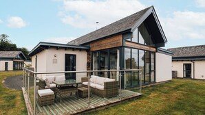 A modern house with a glass-enclosed patio, outdoor furniture, and a grassy lawn. - Betony (Bamburgh)