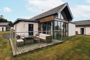 Una casa moderna con un patio de cristal, muebles de exterior y un césped.
