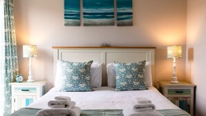 A neatly made bed with pillows, two bedside tables with lamps, and a wall clock on one table. - Betony (Bamburgh)