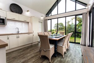 Una cocina moderna con armarios blancos, una mesa de comedor preparada para cuatro personas y un ventanal con vistas a la vegetación.