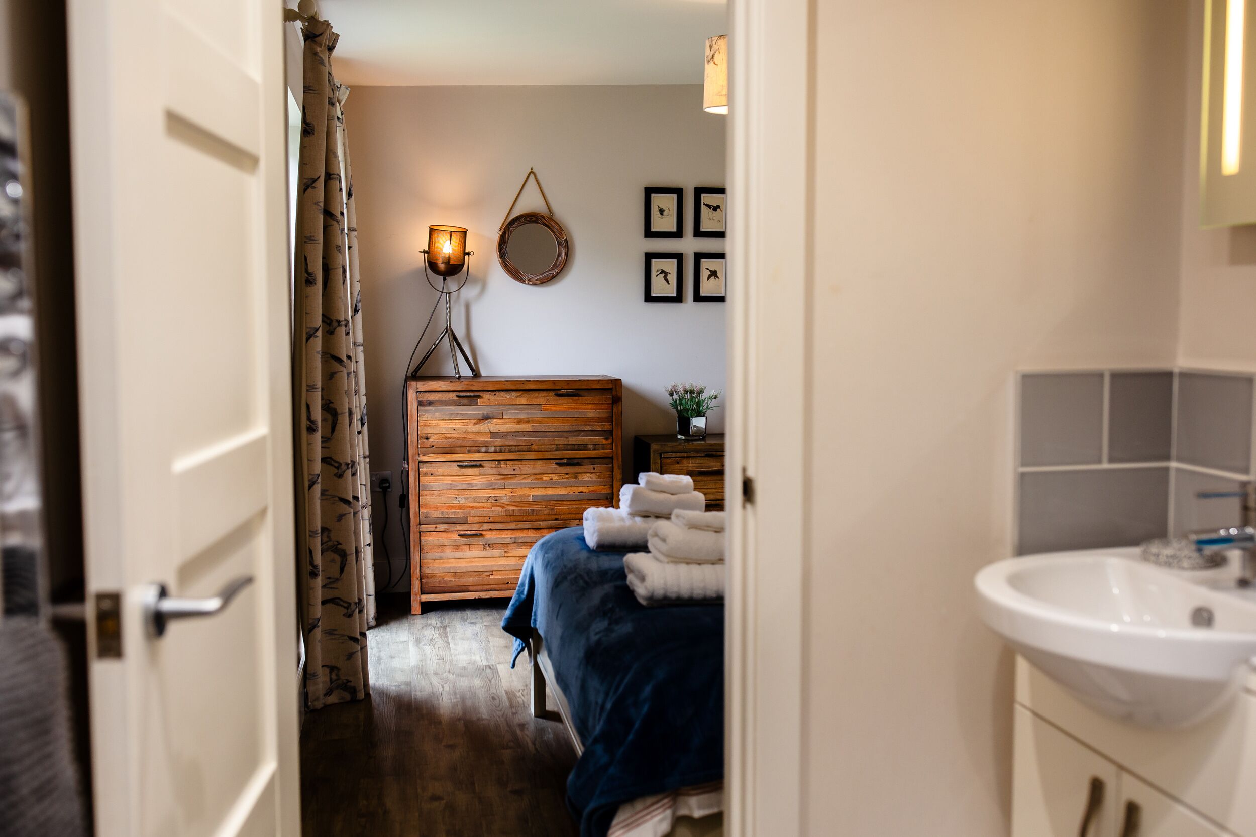 A bedroom with a wooden headboard, a bedside table with a lamp, and a wall-mounted mirror.