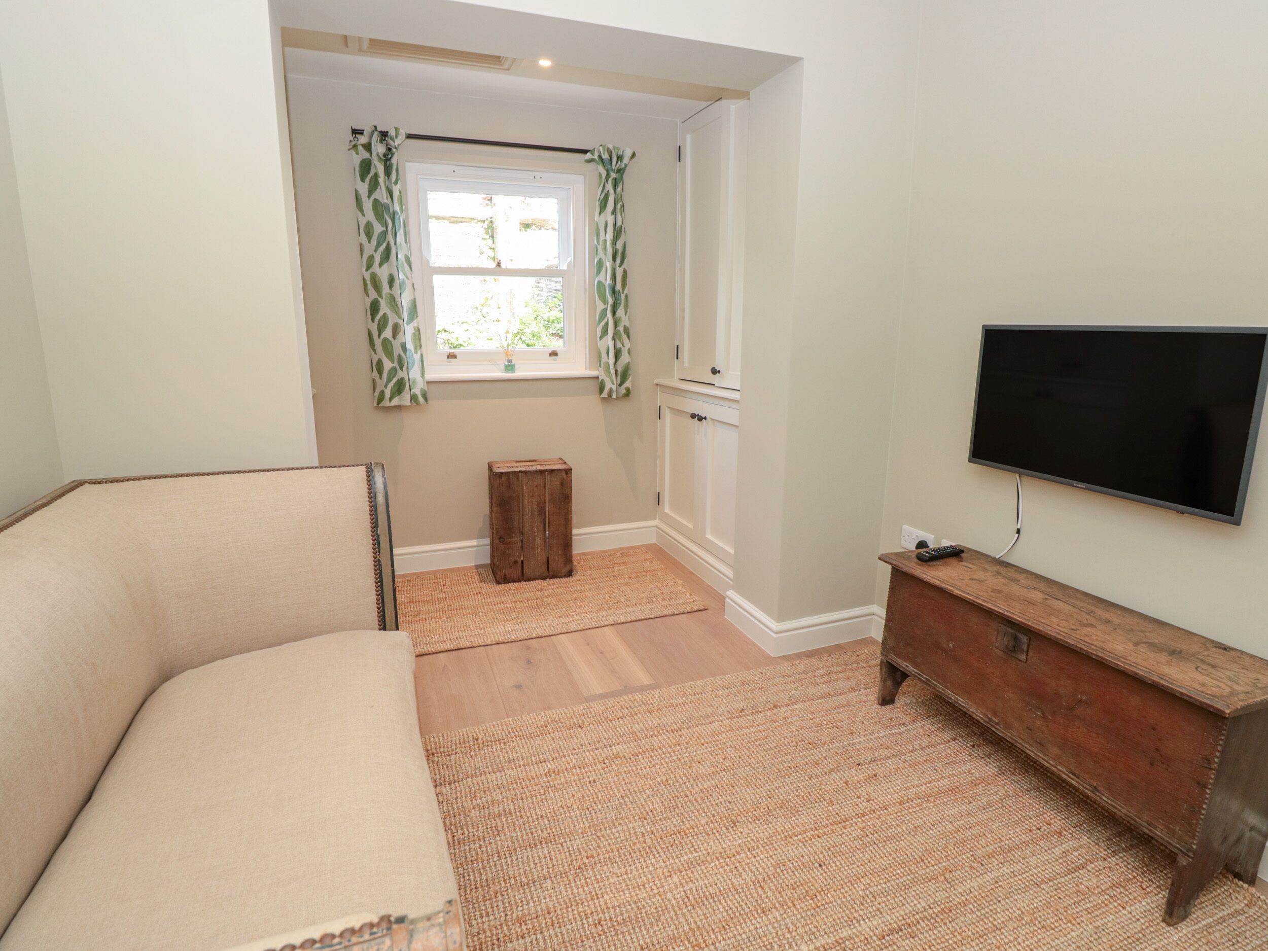A room with a sofa, a wooden cabinet, a television, a window with curtains, and a small stool.