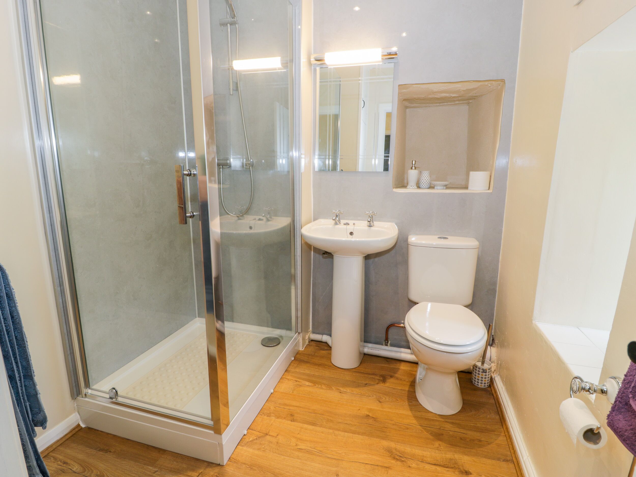 A bathroom with a glass shower enclosure, a pedestal sink, a toilet, and a mirror above the sink.