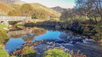 A river with a stone bridge, surrounded by lush greenery and hills.