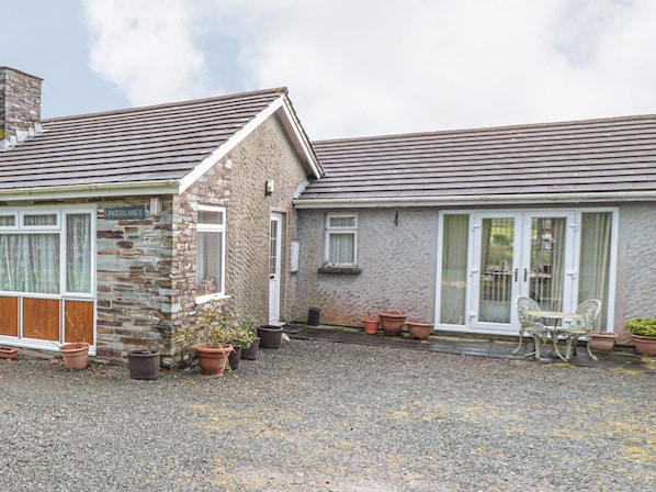 A stone building with a gravel driveway, potted plants, and a patio with outdoor furniture. - Little Lanes (Camelford)