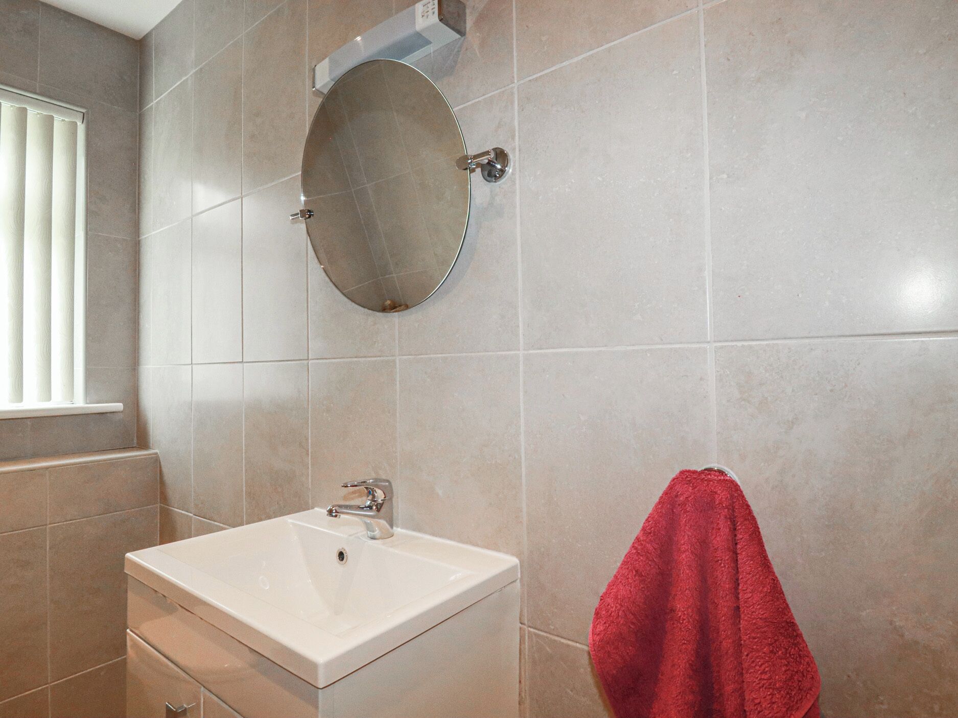 A bathroom with a white sink, a round mirror, and a red towel hanging on the wall.