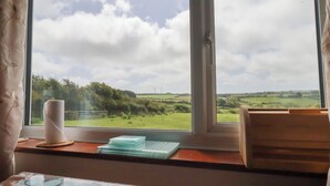 A room with a large window, a table with a tissue roll, a stack of plates, and a chair. - Little Lanes (Camelford)