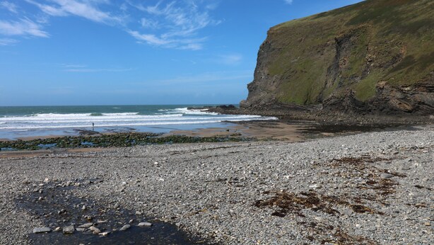 A rocky beach with a cliff, ocean waves, and a clear sky. - Little Lanes (Camelford)