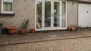 A house with a garage door, a window, and potted plants on the front. - Little Lanes (Camelford)