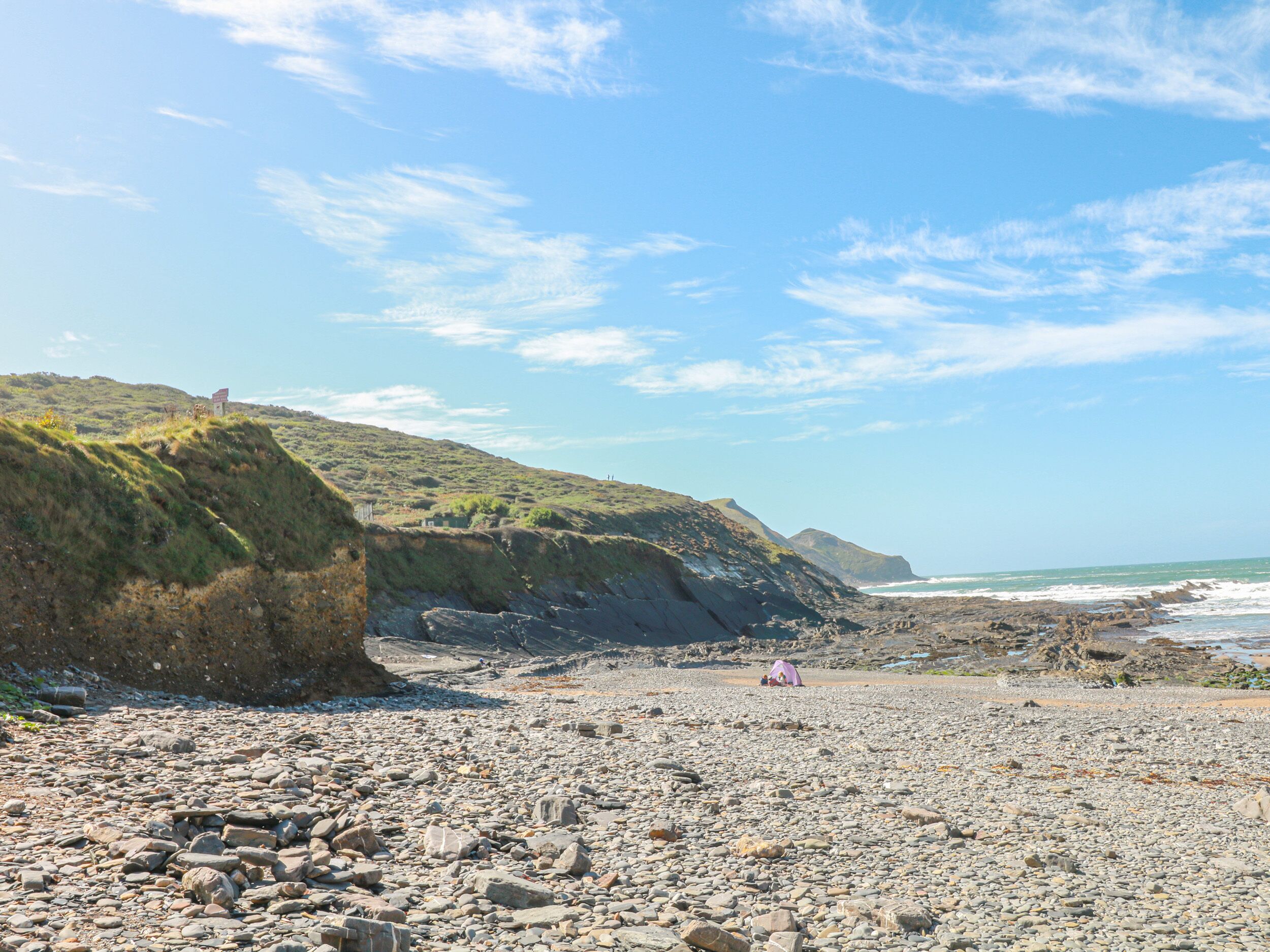 A rocky beach with a tent and a grassy hill in the background.