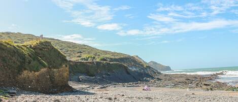 A rocky beach with a tent and a grassy hill in the background.