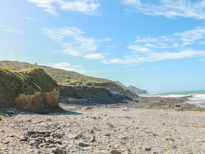 A rocky beach with a clear sky and distant hills. - Little Lanes (Camelford)