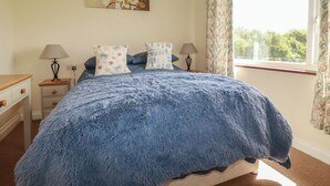 A bedroom with a bed, two bedside tables, lamps, a painting, and a window with curtains. - Little Lanes (Camelford)