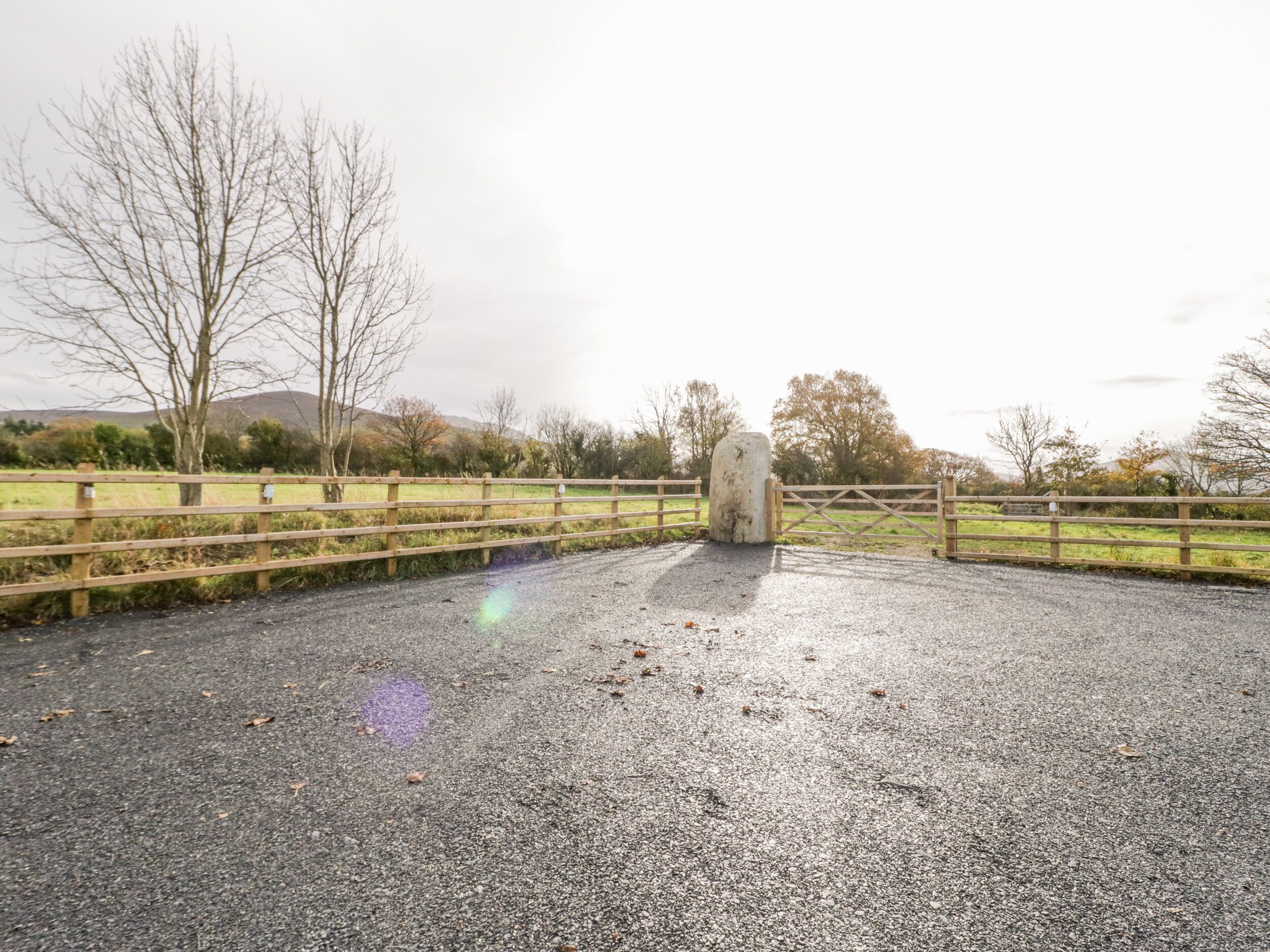 A gravel path leading to a wooden gate with a stone pillar in the center.