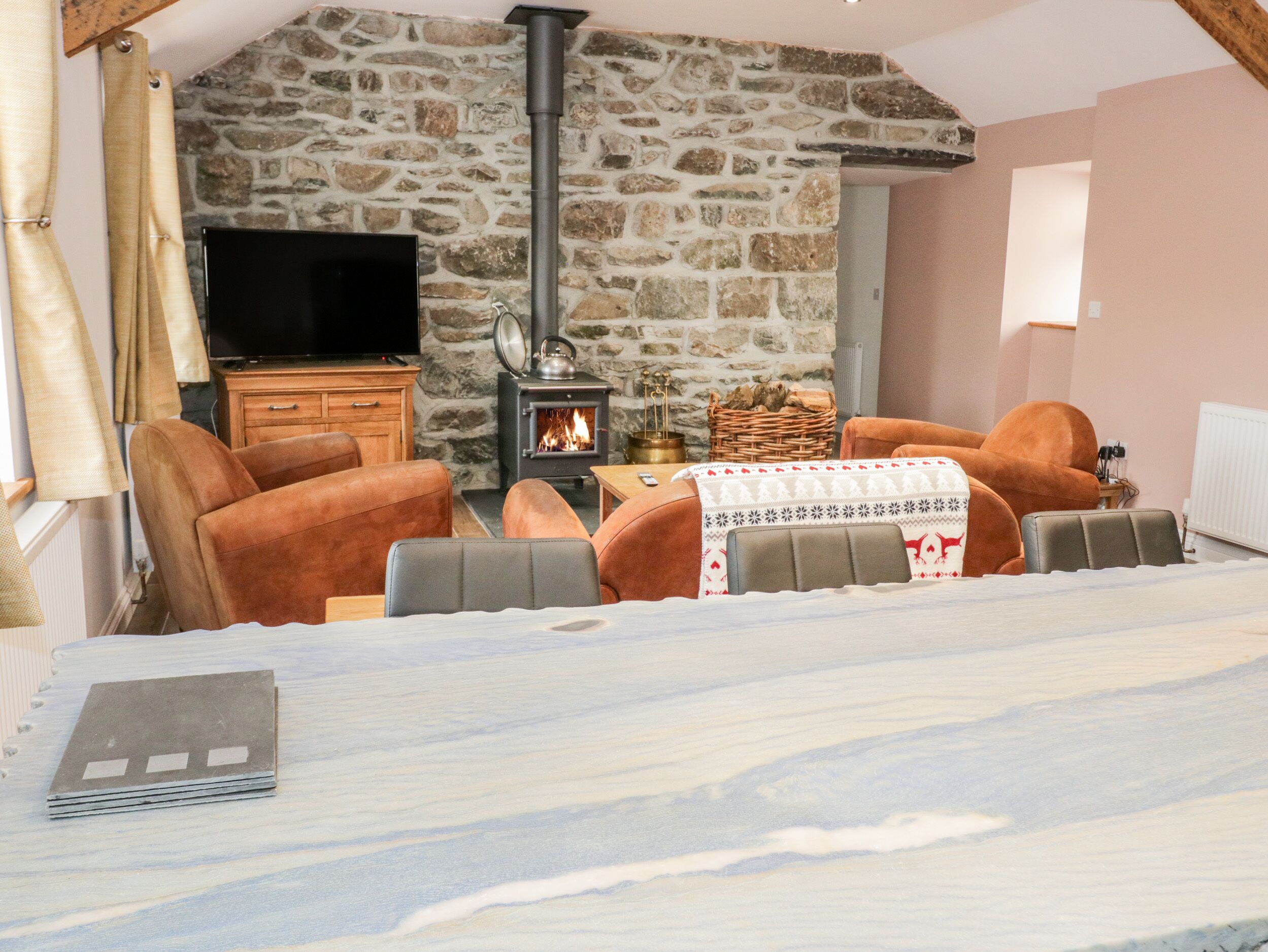 A cozy room with a stone wall, a fireplace, leather sofas, and a flat-screen TV.