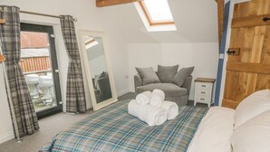 A bedroom with a bed, a nightstand, a grey sofa, a wooden wardrobe, and a skylight.