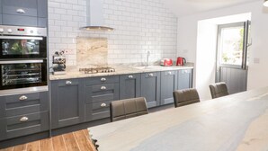 A modern kitchen with grey cabinets, a marble backsplash, and a dining area with a large table and chairs.