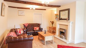 A living room with a leather sofa, a wooden coffee table, a fireplace, and a red rug. - Stone Farm Cottage (Sheffield)