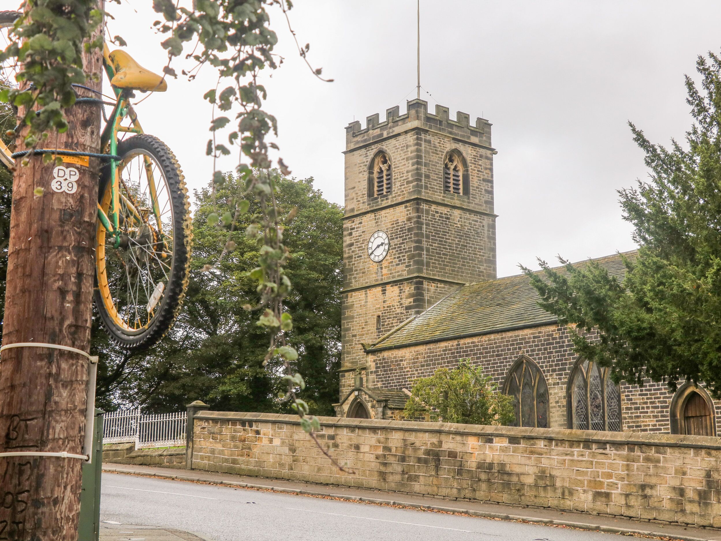 A historic church with a clock tower, a stone wall, and a bicycle parked against a tree.