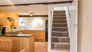 A kitchen with wooden cabinets, a black countertop, and a built-in island. There is a staircase leading to another level. - Stone Farm Cottage (Sheffield)