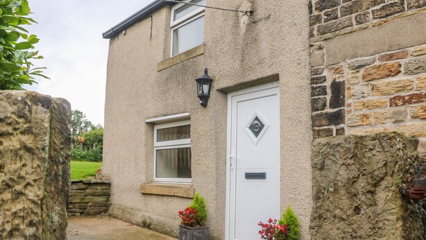 A stone house with a white door, a window, and a small garden area with potted plants. - Stone Farm Cottage (Sheffield)