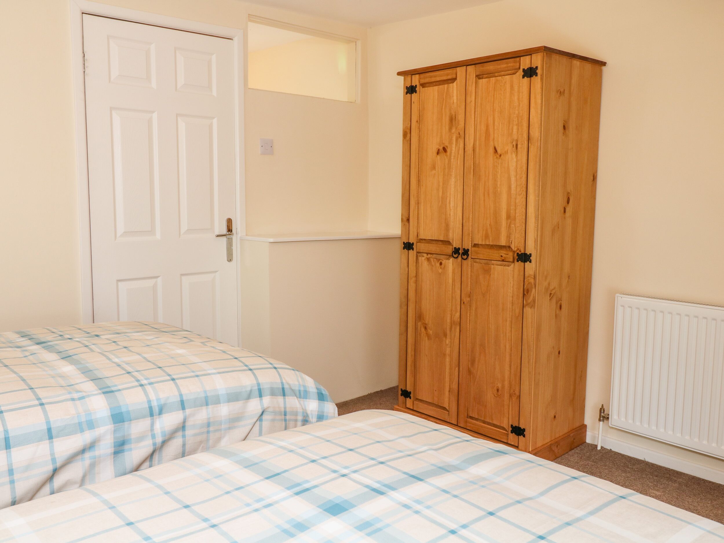 A bedroom with two beds, a wooden wardrobe, a white door, and a radiator.