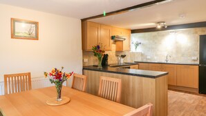 A modern kitchen with wooden cabinets, a central island, and a dining area with a wooden table and chairs. - Stone Farm Cottage (Sheffield)