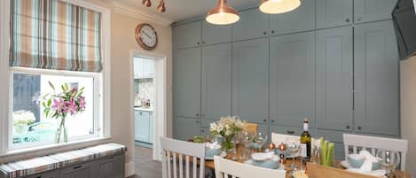 A dining area with a wooden table set for four, a window with a view, and a kitchen in the background.