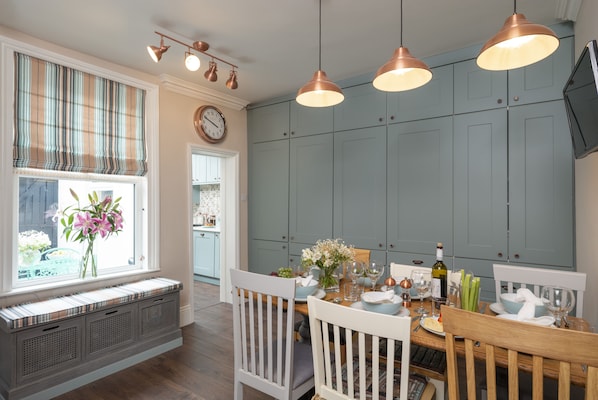 A dining area with a wooden table set for four, a window with a view, and a kitchen in the background. - See Glympse (Whitby)