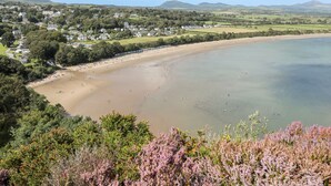 A coastal town with a sandy beach, houses, and hills in the background. - Songbird Hideaway (Pwllheli)