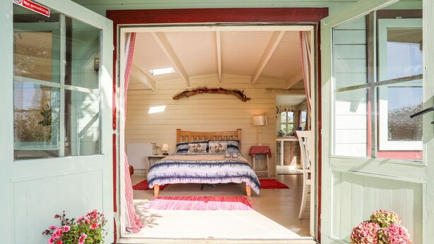 A bedroom with a bed, a nightstand, a lamp, and a window. - Songbird Hideaway (Pwllheli)