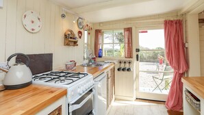 A kitchen with a gas stove, oven, and wooden countertop. There is a window with a view of the outside. - Songbird Hideaway (Pwllheli)