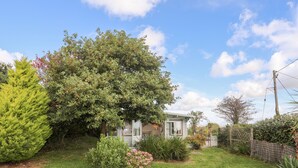 A residential property with a well-maintained lawn, a variety of shrubs, and a large tree providing shade. - Songbird Hideaway (Pwllheli)