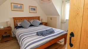 Ein Schlafzimmer mit einem hölzernen Bett, gestreifter Bettwäsche, zwei gerahmten Bildern an der Wand, einer Nachttischlampe und einem Holzschrank.