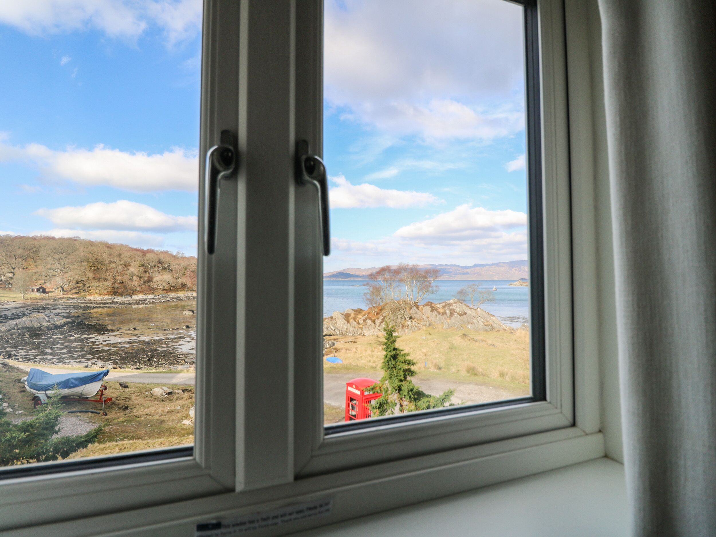 Ein Fenster mit Seeblick, ein roter Sessel und ein Boot mit Plane.