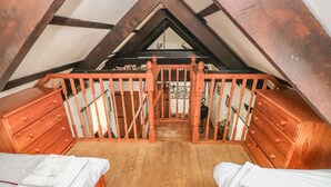 A loft bedroom with wooden floors, a sloped ceiling, and a wooden railing. - Bluebell Cottage (Milford Haven)